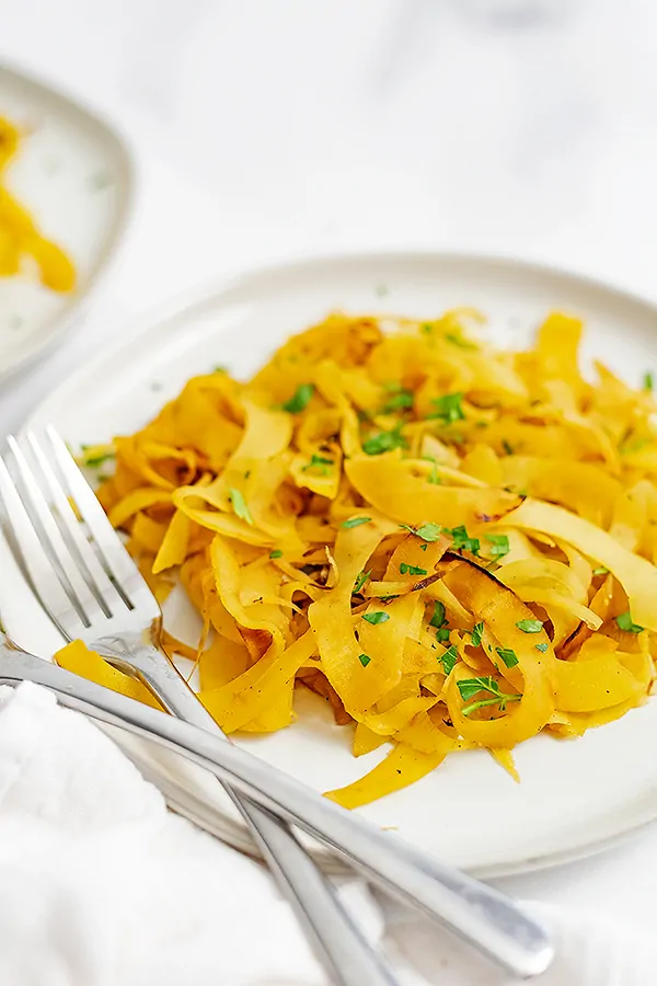 Plate filled with simple spiralized rutabaga recipe with two forks on the left side of the plate and a white napkin besides the forks