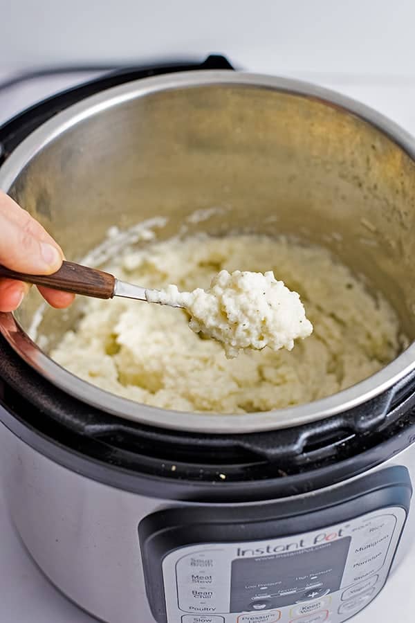 Spoon holding a spoonful of vegan garlic mashed cauliflower over the instant pot