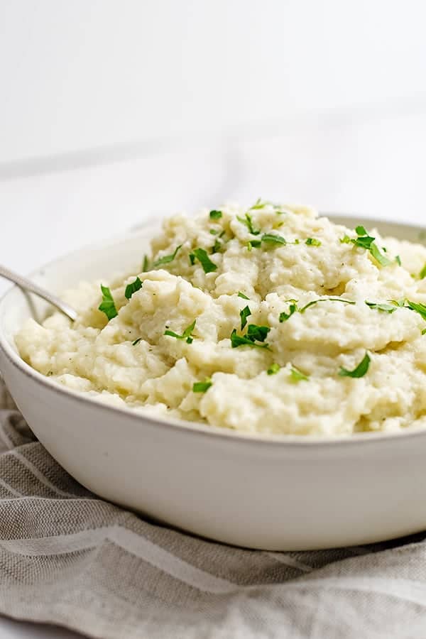 Large bowl of vegan garlic mashed cauliflower over a grey striped napkin with a spoon in the bowl 