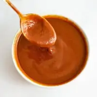 White bowl of Whole30 BBQ Sauce with a spoon full of bbq lifting from the bowl.