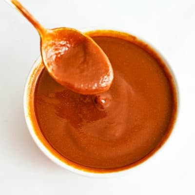 White bowl of Whole30 BBQ Sauce with a spoon full of bbq lifting from the bowl.