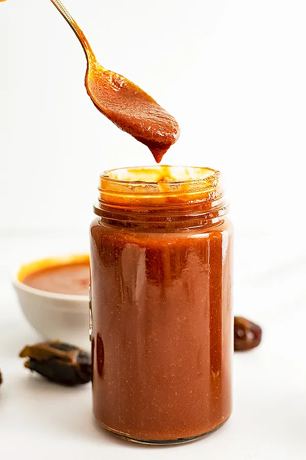 Large jar of Whole30 BBQ sauce with a spoon full of BBQ over the jar and dates in the background