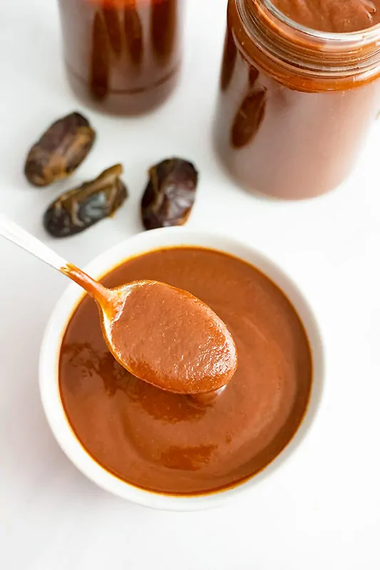 White bowl of Whole30 BBQ Sauce with a spoon full of bbq lifting from the bowl.
