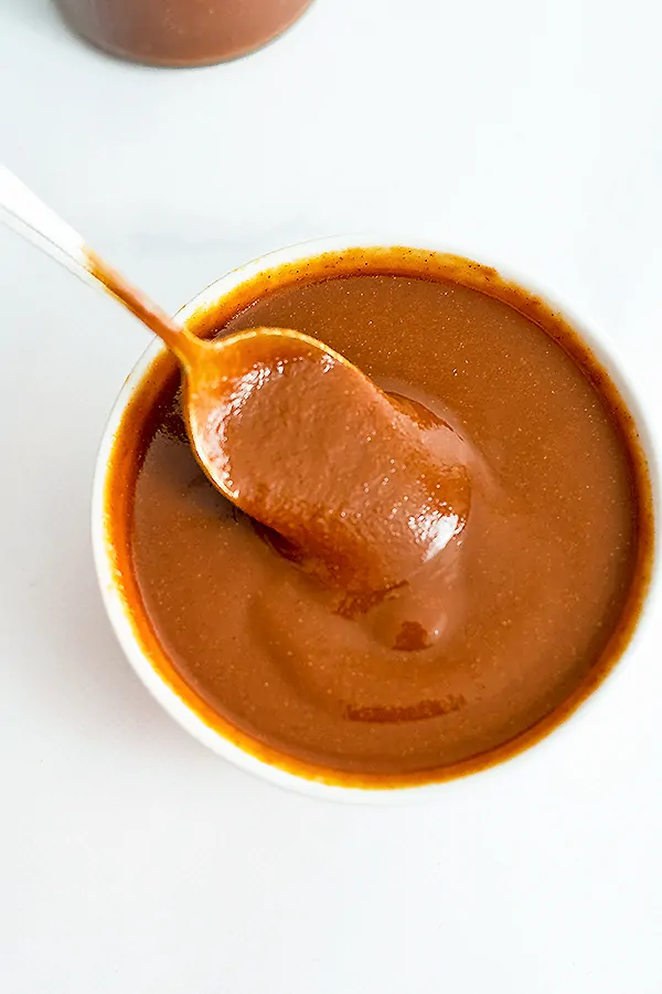 White bowl of Whole30 BBQ Sauce with a spoon full of bbq lifting from the bowl.
