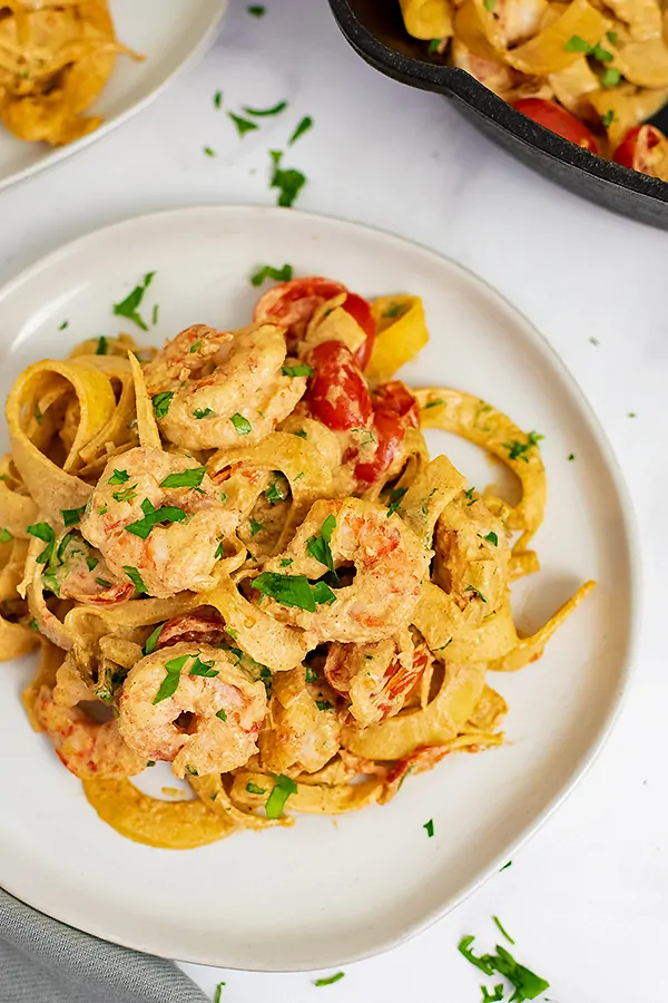 White plate filled with Whole30 Creamy Cajun Shrimp Pasta recipe with fresh parsley and red pepper flakes sprinkled on top