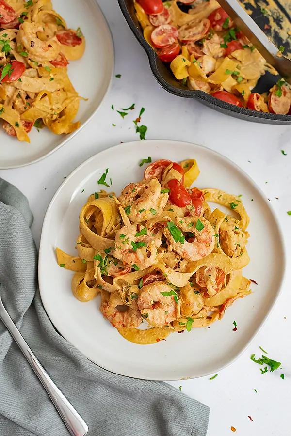 Overhead shot of a white plate filled with Whole30 Creamy Cajun Shrimp Pasta recipe with a second plate in the background and a grey napkin and a fork to the left of the plate