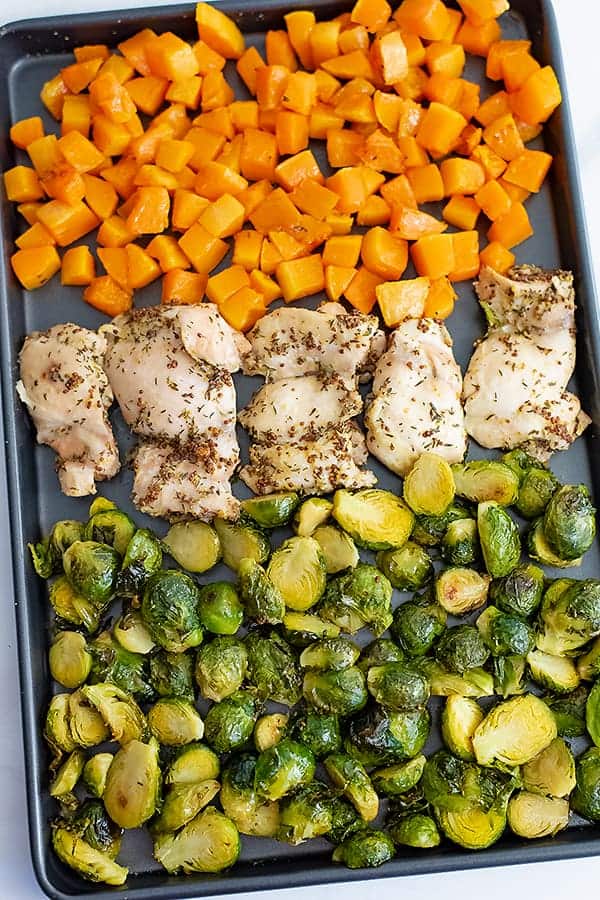 Sheet pan filled with butternuts squash cubes, dijon mustard chicken thighs and halved brussel sprouts