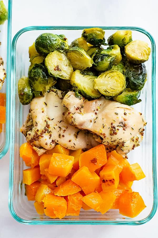 Pyrex container filled with meal prepped sheet pan dijon mustard chicken and vegetables ( brussel sprouts and butternut squash)