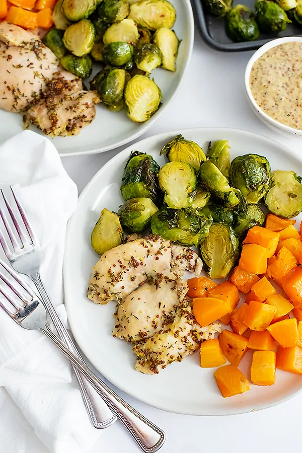 Overhead shot of plate filled with sheet pan dijon mustard chicken thighs and veggies with two forks to the left of the plate over a white napkin
