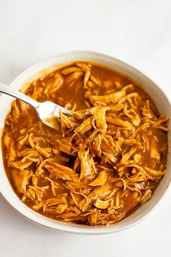 Large bowl filled with instant pot bbq chicken with a fork holding the shredded chicken over the bowl. 
