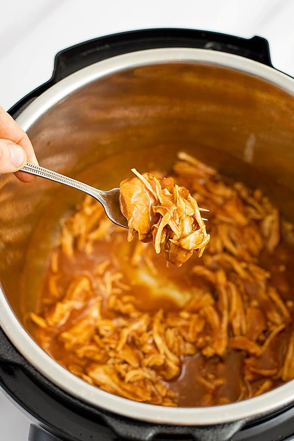 Instant pot full of instant pot bbq chicken with a fork holding up the shredded chicken over the instant pot. 