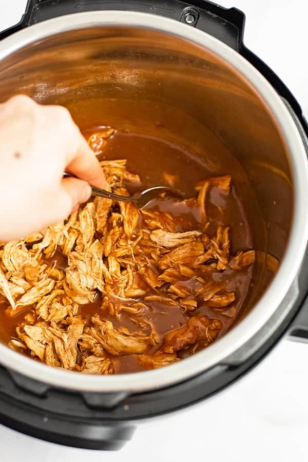 Instant pot BBQ chicken recipe in the instant pot. The shredded chicken is being stirred into the sauce. 