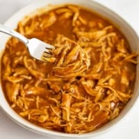 Large bowl filled with instant pot bbq chicken with a fork holding the shredded chicken over the bowl.