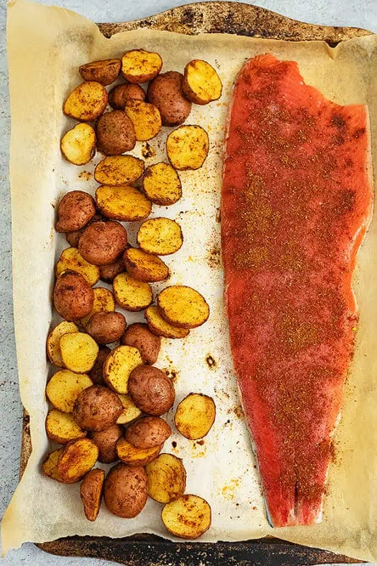 Cajun potatoes and salmon on a baking sheet with cajun seasoning on the salmon.