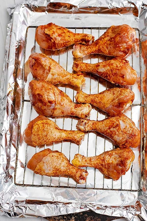 Raw chicken drumsticks on a baking rack over a foil lined baking sheet