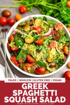 Overhead shot of a large white bowl filled with Greek Spaghetti Squash Salad. Tomatoes and parsley surround the bowl and there is a white napkin and two forks off to the left. Pinterest text on the bottom of the photo