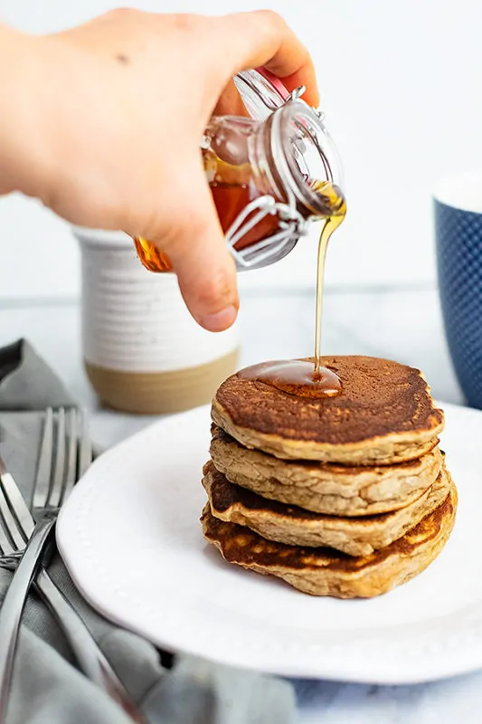 Hand pouring syrup over gluten free protein pancakes