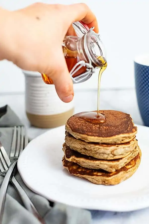 Hand pouring syrup over gluten free protein pancakes 