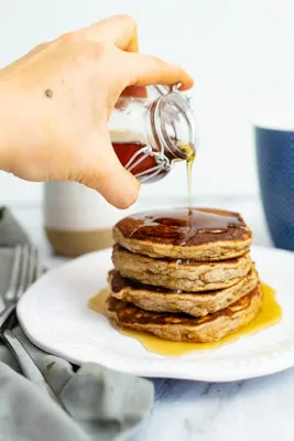 Stack of gluten free protein pancakes with syrup dripping down. Blue coffee cup in the background