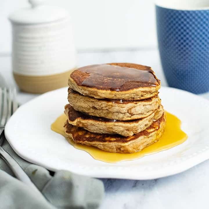 Stack of gluten free protein pancakes with syrup dripping down. Blue coffee cup in the background