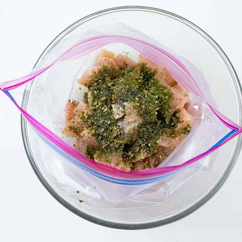 Open zip lock bag with raw chicken and spices over the chicken,