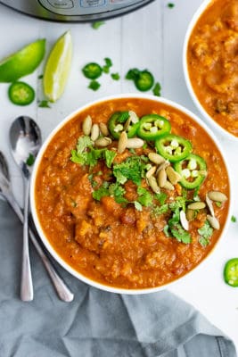 Overhead shot of large bowl filled with spicy sweet potato soup topped with sliced jalapeno, pumpkin seeds and chopped cilantro. Spoon resting on the left side of the bowl