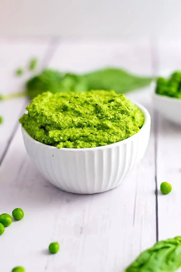 Close up shot of the bowl of pea pesto with basil in the background
