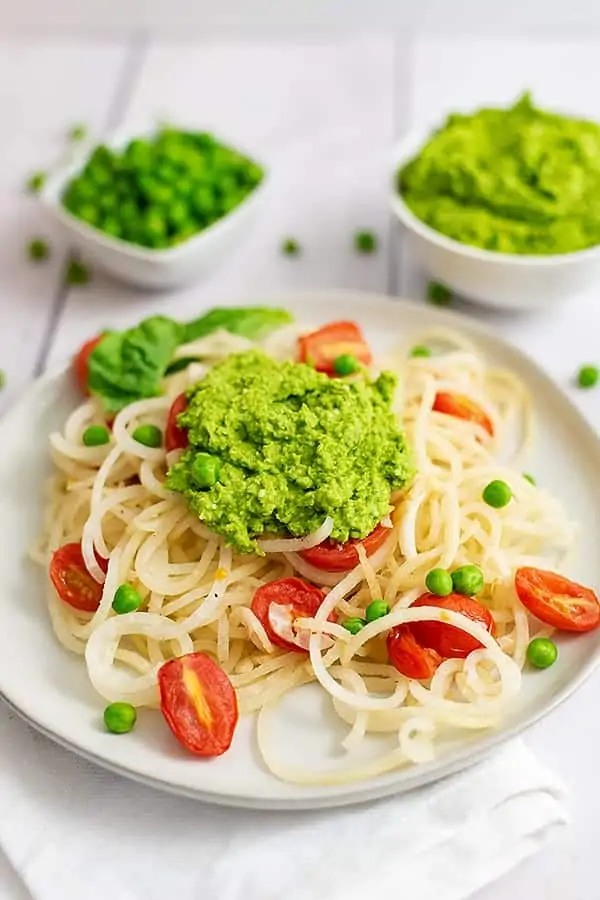 Overhead shot of a plate filled with pasta and tomatoes topped with pea pesto