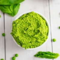 Overhead shot of a bowl filled with pea pesto with peas and basil leaves around the bowl