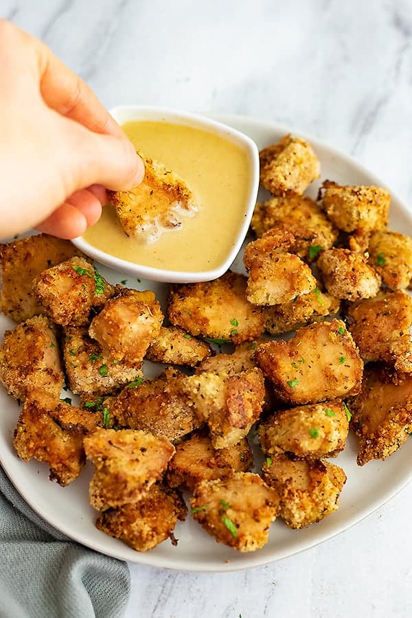 Air fryer chicken nuggets being dipped in honey mustard dressing