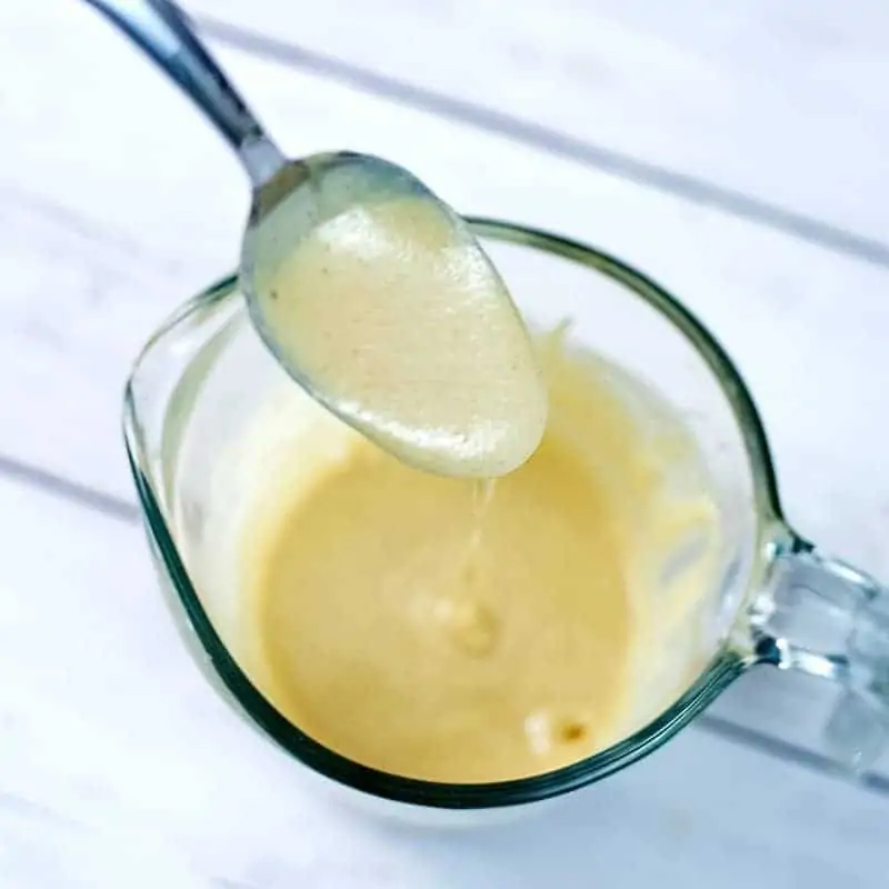 Glass measuring cup filled with lemon tahini dressing. Spoon filled with dressing over the measuring cup