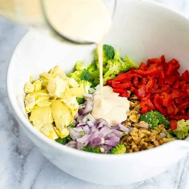 Glass measuring cup filled with lemon tahini dressing being poured over crunchy salad ingredients.