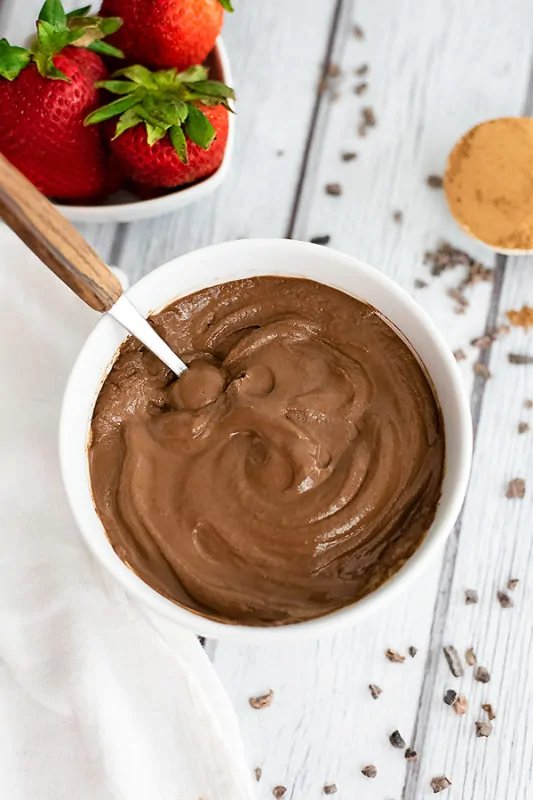 Overhead shot of a white bowl filled with chocolate protein pudding with cacao nibs surrounding the bowl