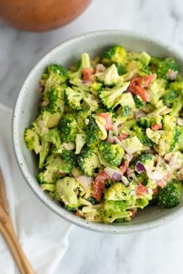 Overhead shot of a bowl filled with crunchy broccoli salad with lemon tahini dressing. White napkin to the left of the bowl