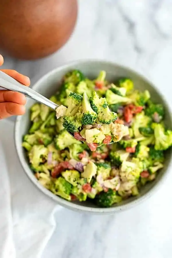 Overhead shot of a bowl filled with crunchy broccoli salad with lemon tahini dressing with a spoon being held into the salad bowl