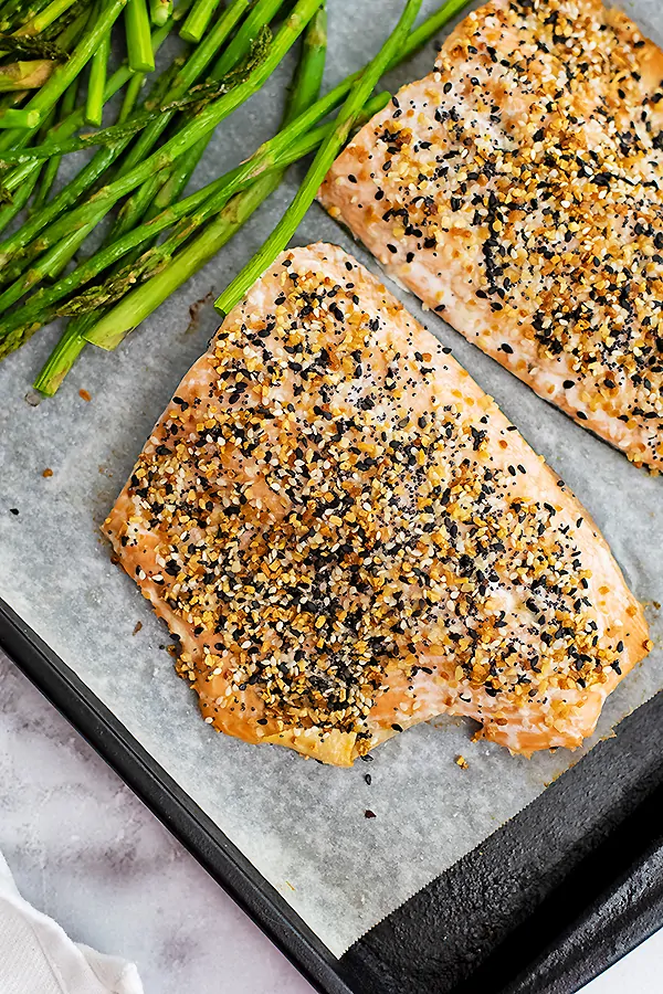 Cooked filet of everything bagel salmon on a baking sheet with asparagus