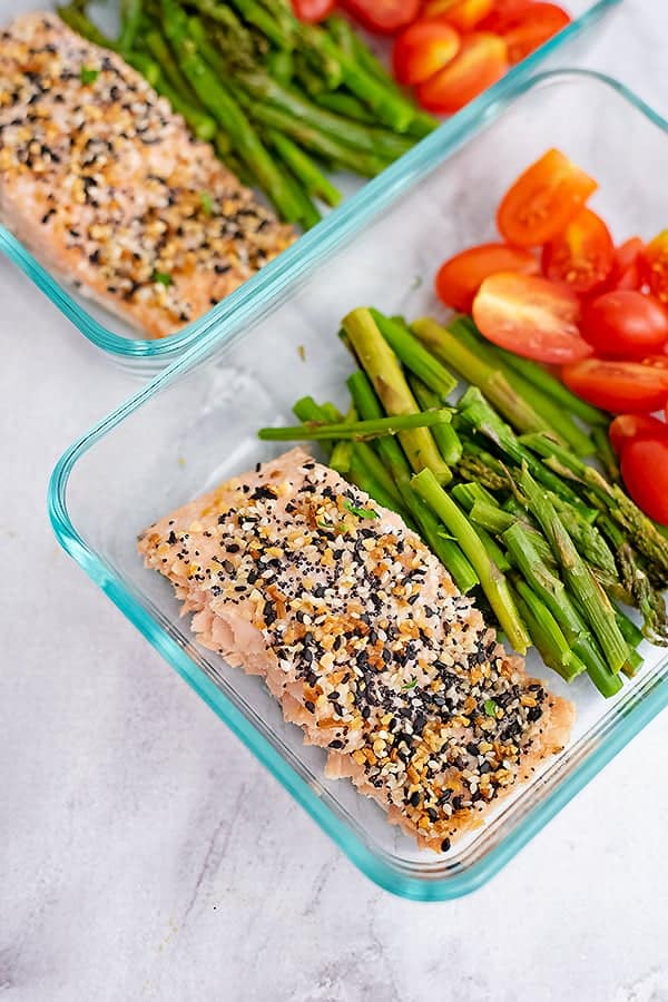 Glass tupperware filled with everything bagel salmon, cooked asparagus and tomatoes