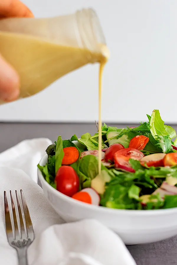Bottle of honey mustard dressing being poured over a salad