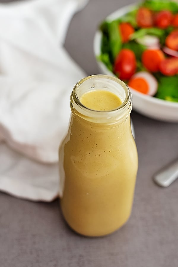 bottle of homemade honey mustard dressing. Salad in the background