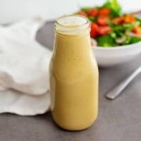 Glass bottle filled with homemade honey mustard dressing recipe with a salad in the background