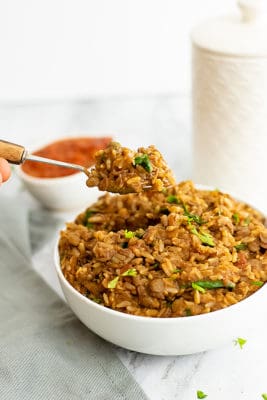 Large bowl of Mexican rice and lentils with a spoon full of the mixture being spooned out of the bowl