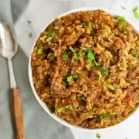 Overhead shot of a large bowl filled with Mexican Rice and Lentils with a spoon to the left of the bowl over a grey napkin