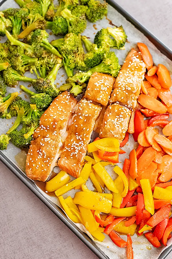 Overhead shot of baked teriyaki salmon and veggies. Sheet pan is tilted so that the entire pan is not in focus.