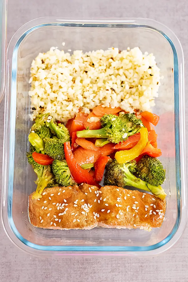 Glass storage container filled with baked teriyaki salmon, mixed veggies and cauliflower rice
