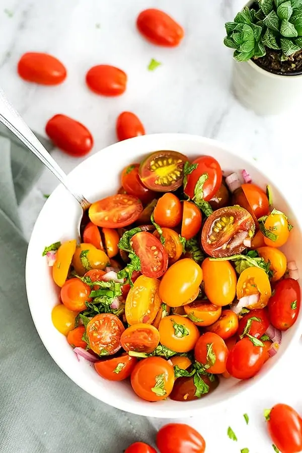 Large white bowl filled with tomato basil salad and a spoon