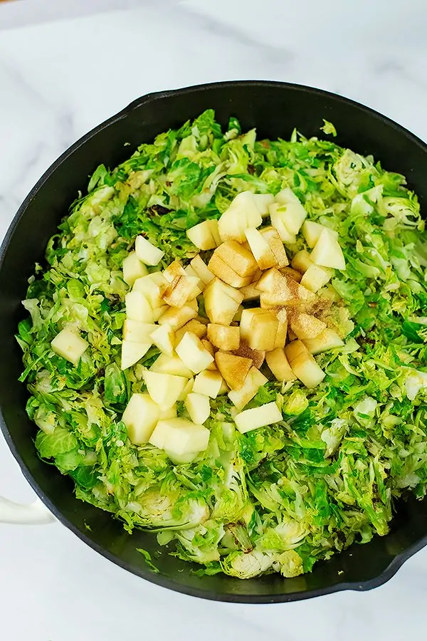 Raw apples and balsamic vinegar added to brussel sprouts in skillet.