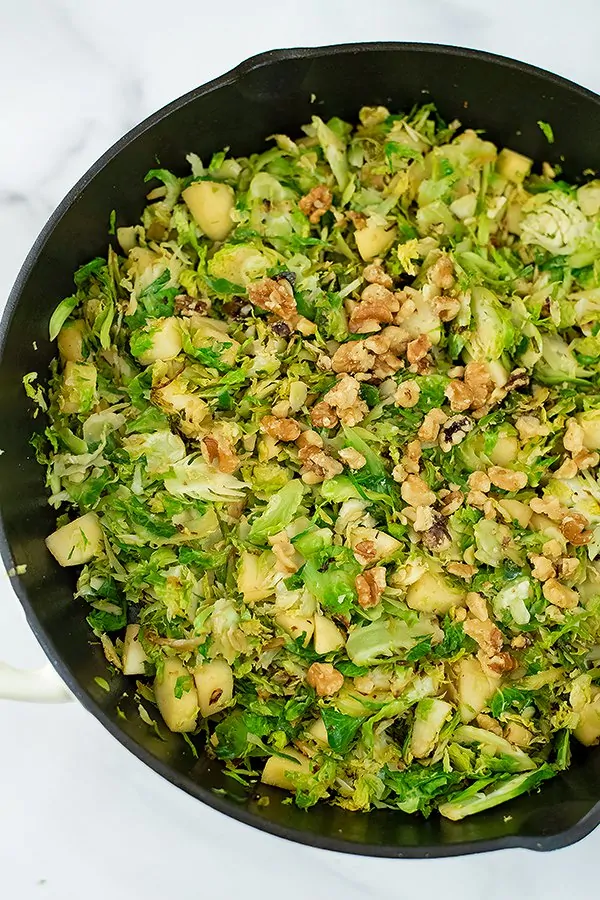 Adding the chopped nuts to the apple brussel sprouts hash in skillet.