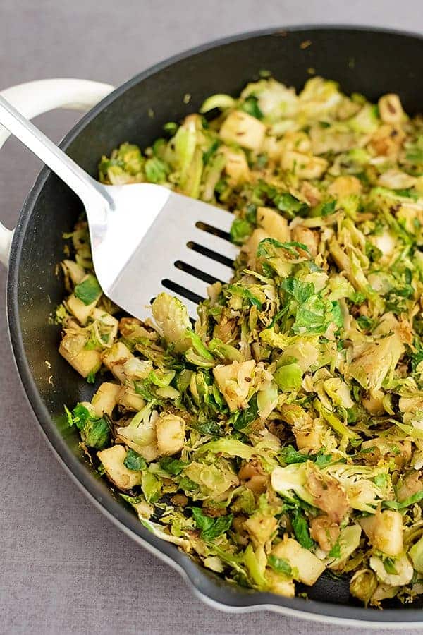 Large skillet filled with apple brussel sprouts hash with a silver spatula