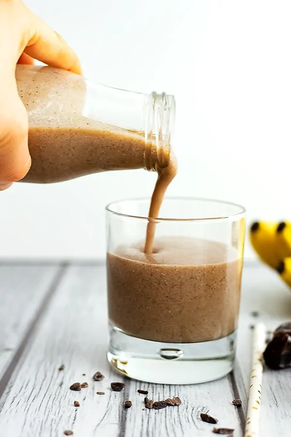 Hand pouring a bottle filled with coffee banana protein smoothie into a glass