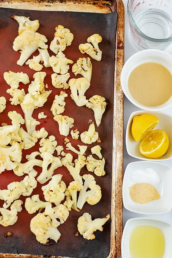 Sheet pan filled with roasted cauliflower. Ingredients to make the hummus in ramekins next to the sheet pan